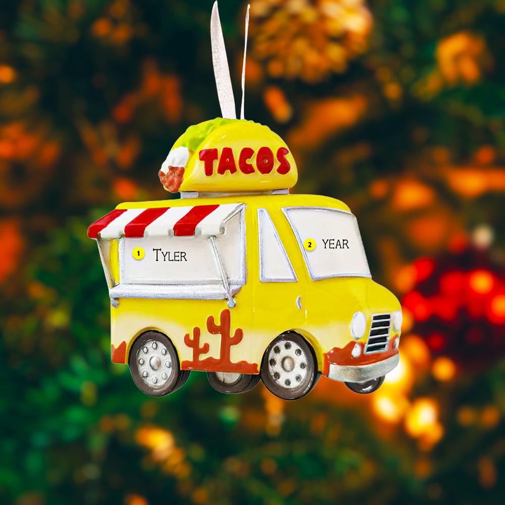 Yellow taco truck ornament with 'TACOS' on top against a blurred Christmas tree background