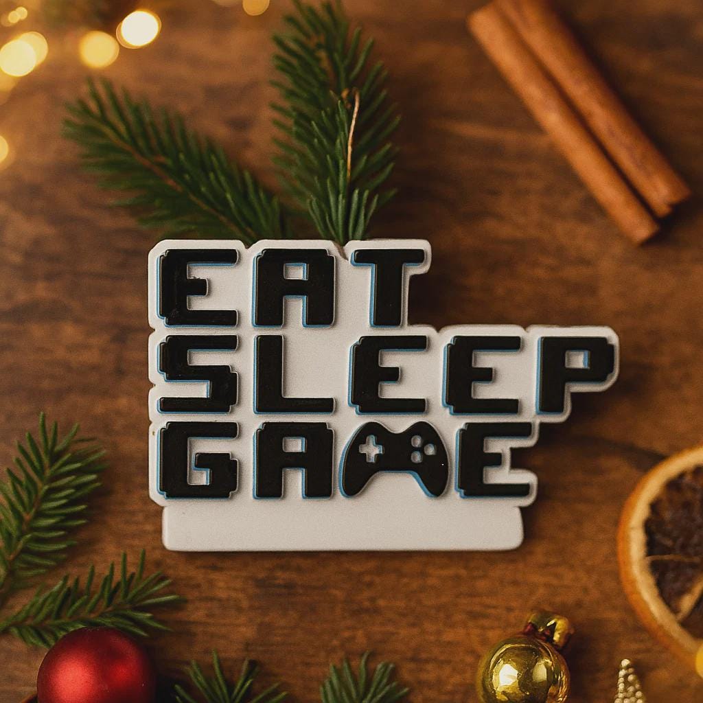 Personalized Eat Sleep Game Christmas ornament with a raised 3D front featuring bold block-style lettering and a detailed game controller icon. The front design is fully three dimensional, creating depth and texture, while the back is flat 2D for easy hanging and durability. White base with black raised letters and subtle colored accents. Includes hand-added personalization with name and year or family name. Gaming-themed holiday ornament displayed on snowy festive background with warm lights, designed for 