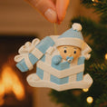 Load image into Gallery viewer, Personalized Baby Boy First Christmas Ornament featuring an adorable baby popping out of a blue gift box with a matching hat and pacifier. The name is displayed on the hat while the year is placed on the ribbon detail, with Baby’s 1st Christmas written along the base. Soft blue and white tones, raised 3D elements, and sweet holiday details make this a charming keepsake. Perfect for newborn boys, baby showers, and celebrating a baby’s very first Christmas season.
