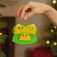 Load image into Gallery viewer, Hand holding a decorative ornament shaped like a family of tacos with a blurred Christmas tree background.
