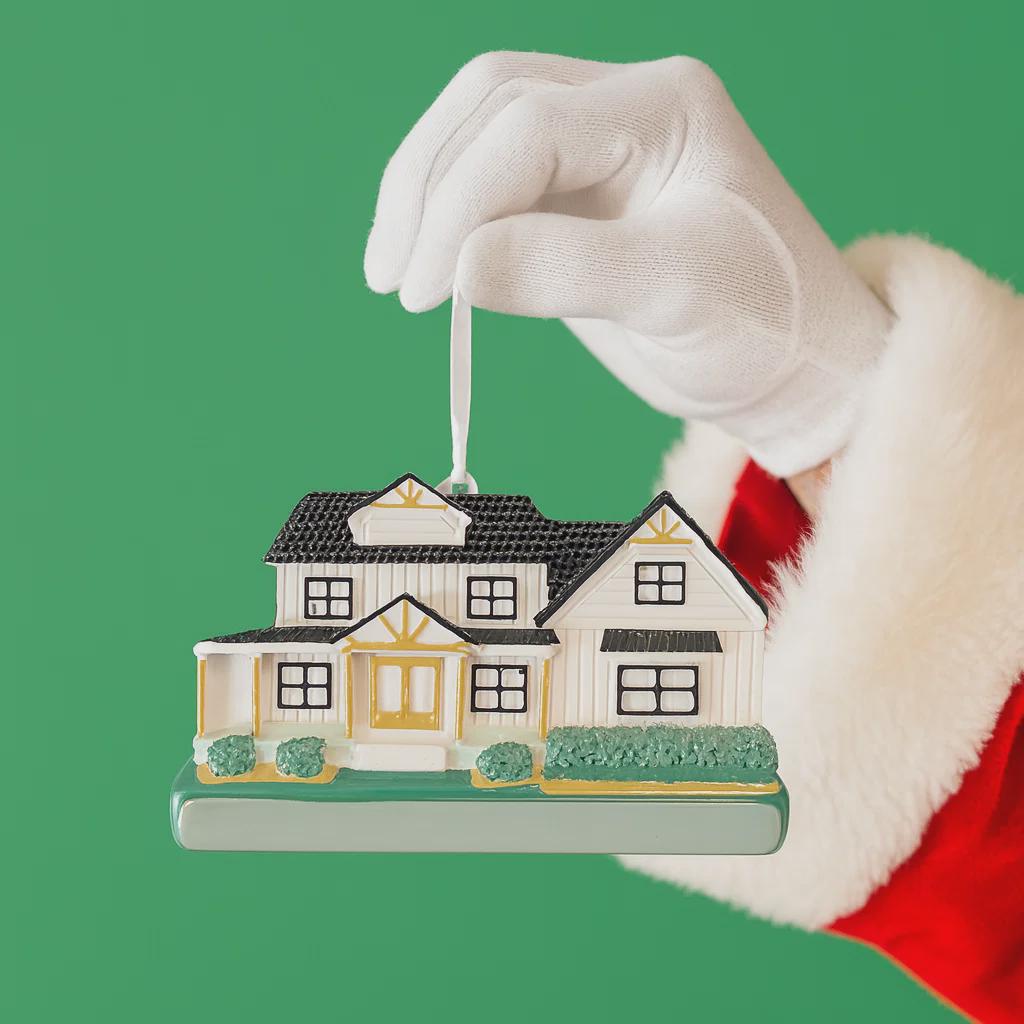 Santa Claus holding a house ornament against a green background