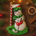 Load image into Gallery viewer, Decorative snowman ornament with golfing equipment on a wooden surface with Christmas decorations.
