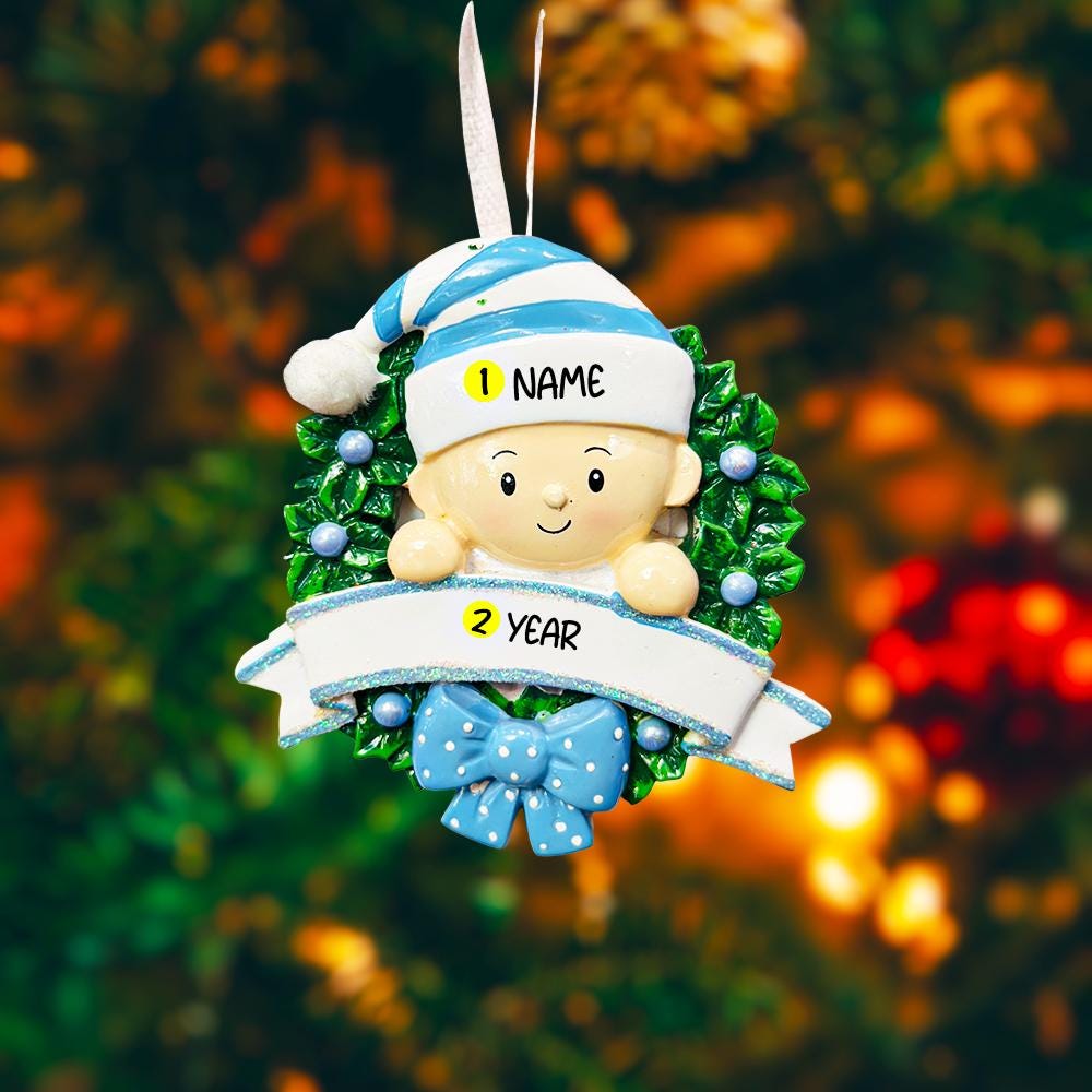 Personalized Baby Boy Christmas Ornament featuring a sweet child peeking from a festive green wreath with blue accents and polka dot bow. This ornament has a raised 3D front design with detailed holly leaves, textured elements, and dimensional lettering. The name is placed on the hat and the year on the banner. A meaningful keepsake for baby’s first Christmas, newborn gift, or holiday memory decoration for the Christmas tree.