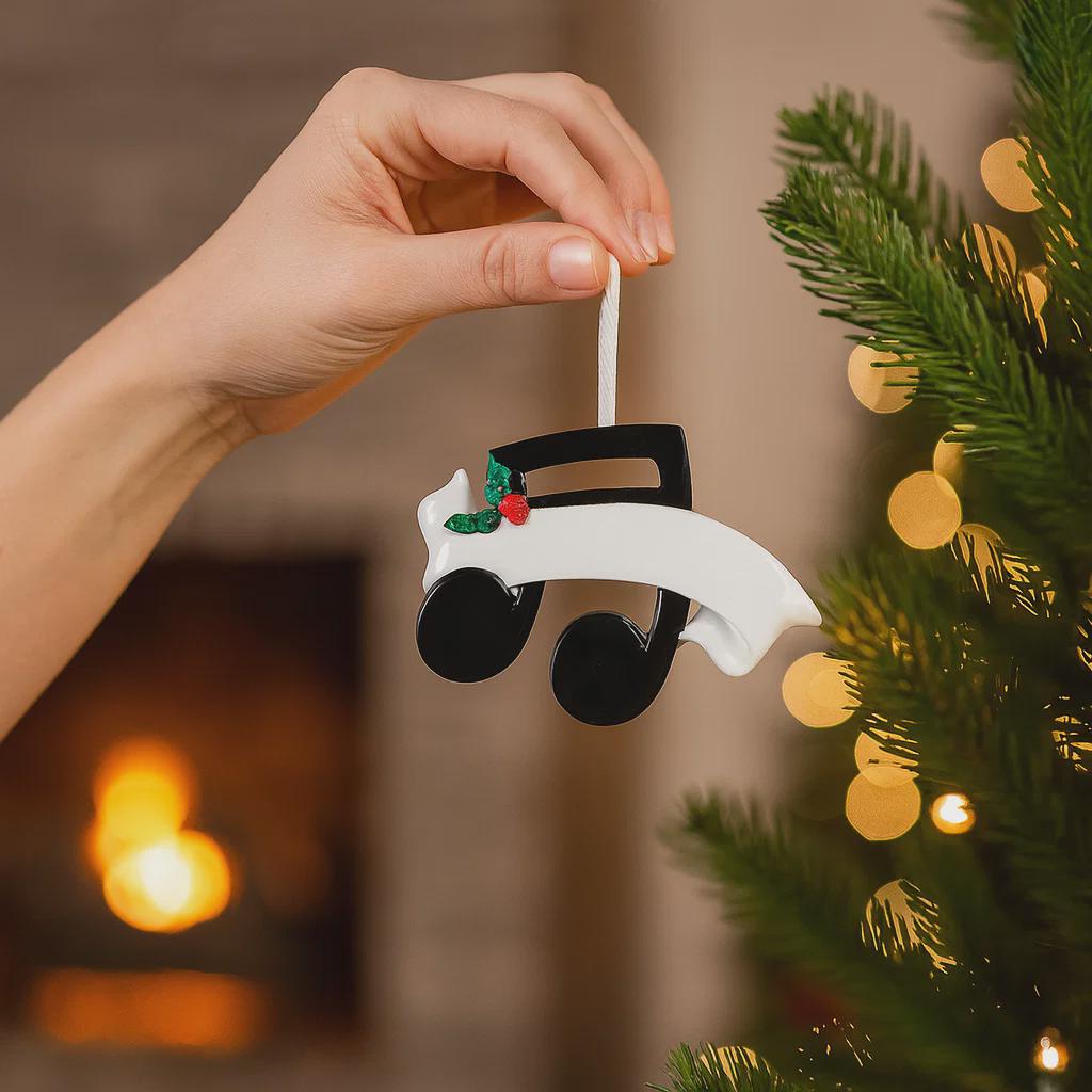 Personalized music note ornament featuring a classic black and white musical note design with subtle holiday accents. Customizable with one name and a year. Crafted from resin with detailed 3D raised front elements and a flat 2D back for balanced hanging. Finished with a glossy surface and satin ribbon. Designed for musicians music students and music themed Christmas tree decor.