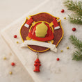 Load image into Gallery viewer, Decorative Christmas ornament with firefighter helmet and fire hydrant charm on a marble surface with festive decorations.
