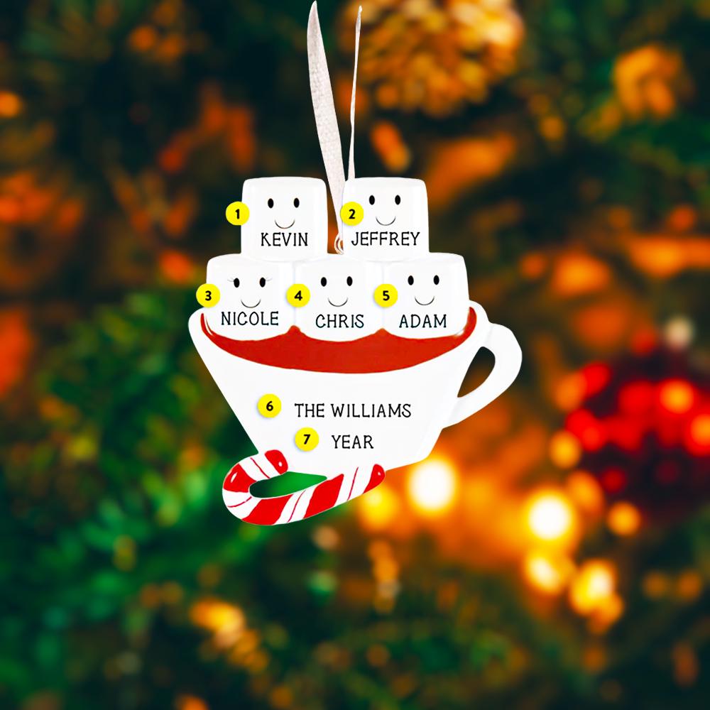 Christmas ornament with names on a cup and marshmallows against a blurred Christmas tree background