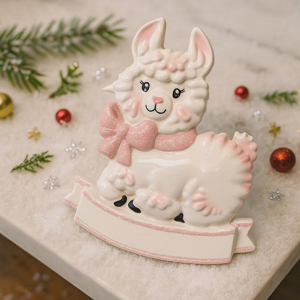 A glossy resin baby girl llama ornament features a white smiling llama with soft pink accents, raised textured fur details, pink bow and scarf elements, glitter highlights, and a smooth painted cartoon style finish, styled with warm holiday lights and nursery themed props, handwritten personalization showing the baby name on the front banner and the year placed on the llama body, designed as a mostly 2D ornament with raised 3D details on the front only.
