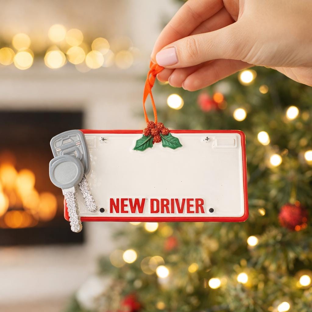 Christmas ornament with 'NEW DRIVER' text and keychain, held by a hand in front of a decorated tree.