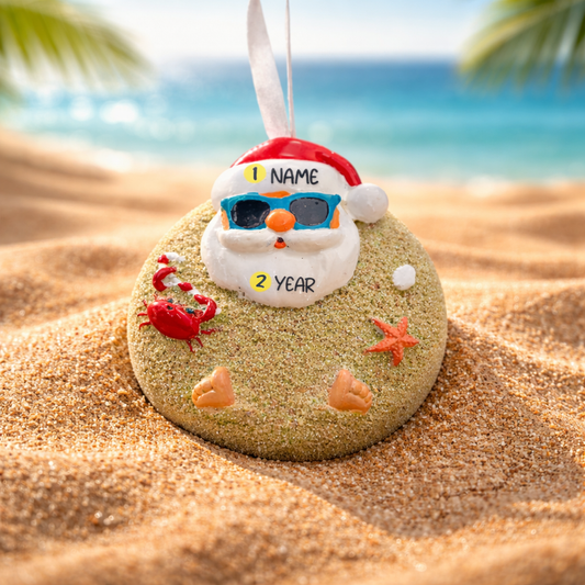 Decorative ornament shaped like a beach ball with a Santa Claus face, sunglasses, and beach elements on sand with ocean background.
