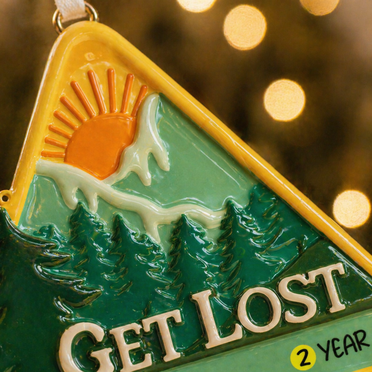 Decorative ornament with a triangle design, sun, trees, and 'GET LOST' text on a blurred light background.