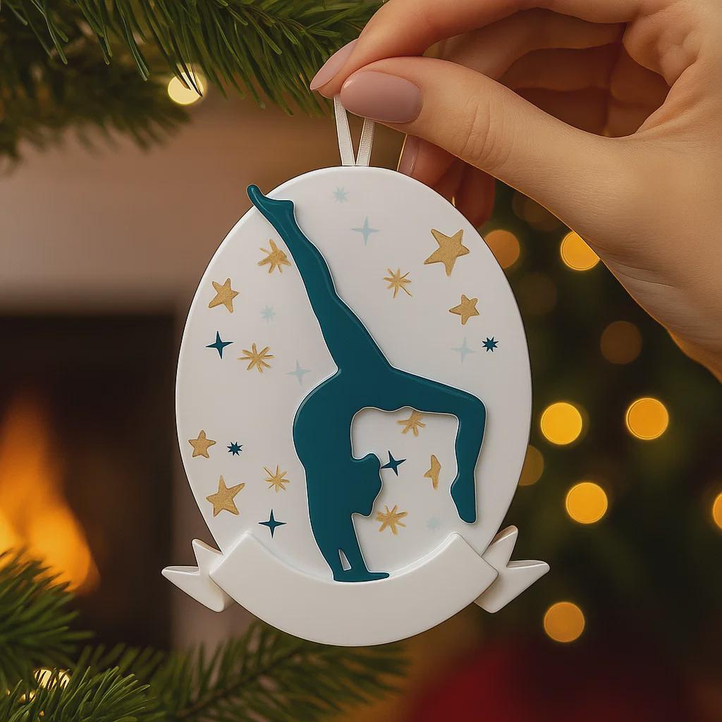 Personalized gymnastics Christmas ornament featuring an oval white design with a navy blue gymnast silhouette performing a handstand pose, surrounded by gold and blue star accents, customizable year displayed on the upper area, customizable name space on the bottom banner, smooth glossy finish with raised 3D front details and flat 2D back, white hanging ribbon, photographed on a soft pink snowy holiday background with winter greenery, festive ornaments, and warm seasonal styling.
