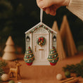 Load image into Gallery viewer, Decorative Christmas ornament shaped like a house with trees and wreath, held against a festive background.
