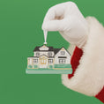 Load image into Gallery viewer, Hand wearing a white glove holding a house-shaped Christmas ornament against a green background
