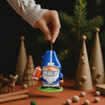 Load image into Gallery viewer, Personalized football gnome Christmas ornament featuring a blue and white gnome character wearing a football helmet and holding a football, customizable name area on the front body and customizable year area on the football, glossy finish with raised 3D front details and flat 2D back, white hanging ribbon, displayed on a snowy football field themed holiday background with pine branches and festive decorations.

