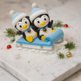 Load image into Gallery viewer, Two penguins on a sled with Christmas decorations on a snowy background

