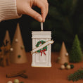 Load image into Gallery viewer, Decorative Christmas ornament with a wreath and ribbon held by a hand against a festive background.
