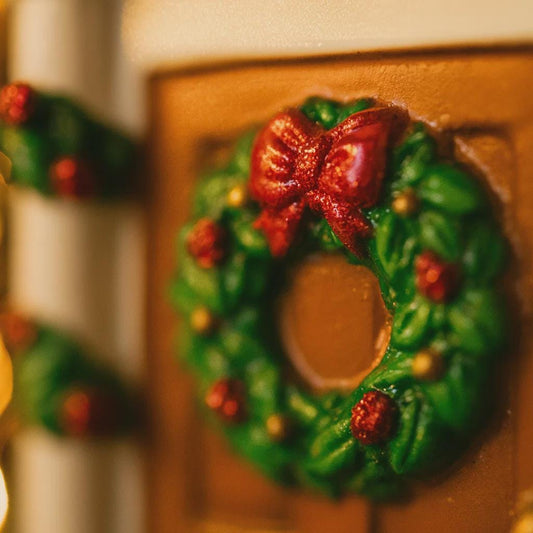 Decorative gingerbread wreath with a red bow on a gingerbread house.