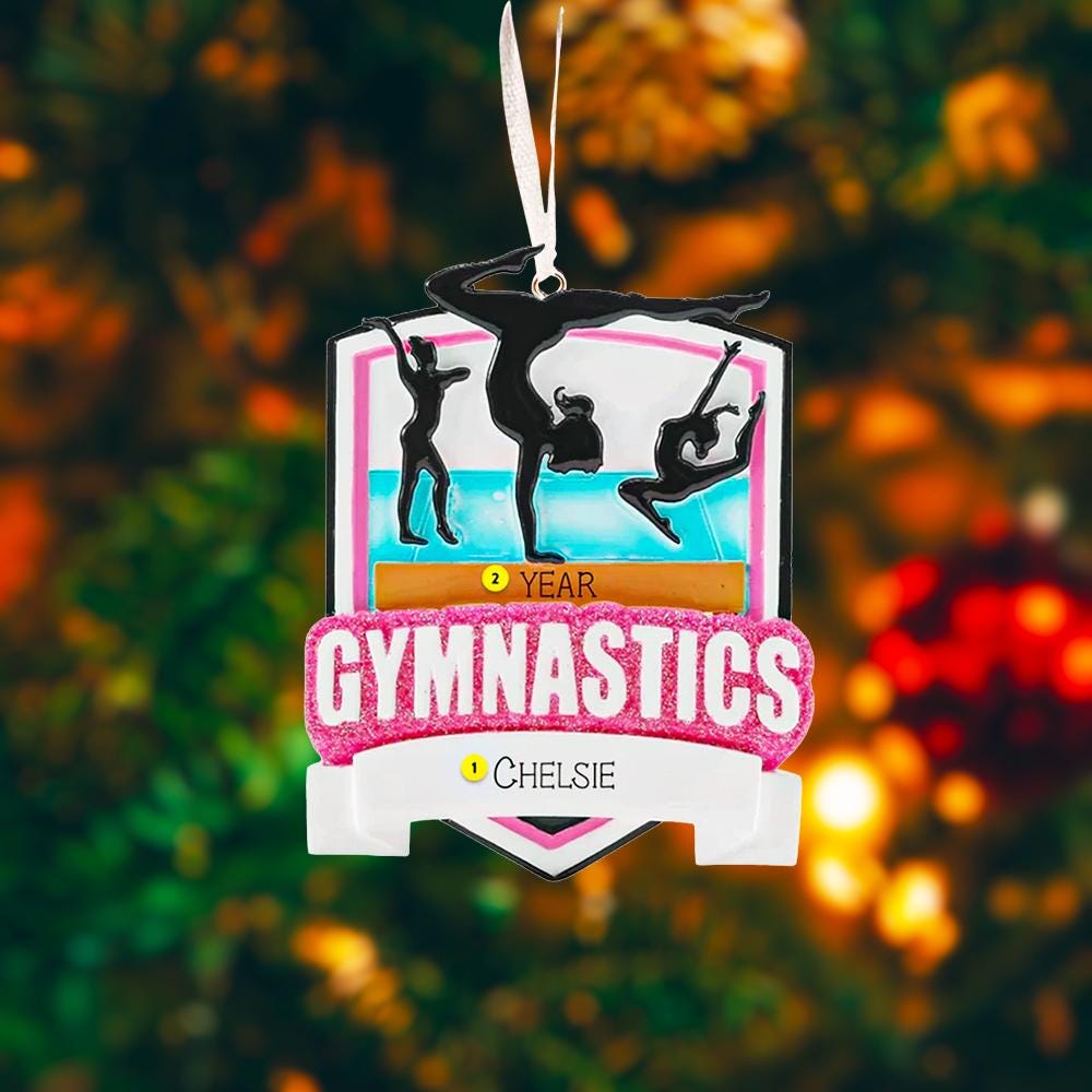 Personalized gymnastics Christmas ornament featuring elegant gymnast silhouette figures in motion, customizable name area on the front banner and customizable year area above the banner, glossy finish with raised 3D front details and flat 2D back, white hanging ribbon, displayed on a soft pink snowy holiday background with festive ornaments greenery and warm Christmas decor.
