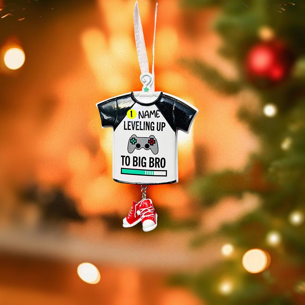 Decorative ornament shaped like a t-shirt with text and a shoe, hanging against a Christmas tree background.