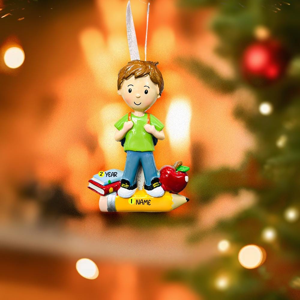 Ornament of a boy with books and an apple, hanging on a decorated tree.