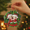 Load image into Gallery viewer, Hand holding a Christmas ornament with couple in red outfits and Santa hats against a blurred Christmas tree background.
