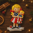 Load image into Gallery viewer, Decorative figurine of two girls in patriotic outfits on a wooden surface with Christmas decorations.
