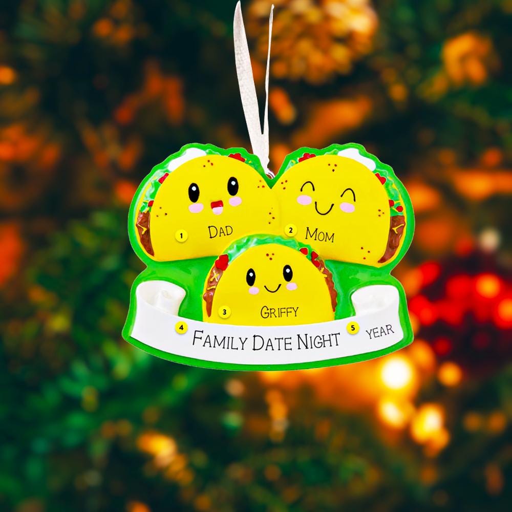 Decorative ornament shaped like a heart with cartoon tacos and text on a blurred Christmas tree background.