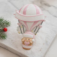 Load image into Gallery viewer, Personalized baby first Christmas ornament featuring a soft pastel pink hot air balloon design with a sweet baby character inside the basket. Handwritten baby name and year or Baby’s First Christmas text displayed on the balloon. Smooth resin finish with gentle glitter accents, nursery themed colors, lightweight structure, mostly 2D ornament with raised 3D details on the front only, designed for baby Christmas tree decor and keepsake gifting.
