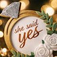 Load image into Gallery viewer, Elegant engagement Christmas ornament featuring gold accents white florals and the phrase she said yes. Personalized with a custom date to commemorate a proposal or engagement moment. A romantic keepsake perfect for celebrating newly engaged couples weddings and meaningful holiday memories.
