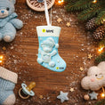 Load image into Gallery viewer, A glossy resin baby boy stocking ornament features a soft pastel blue Christmas stocking shape with a raised glitter style baby figure on the front, white cuff detail, small star accents, and smooth painted surfaces, surrounded by warm holiday lights and nursery themed props, handwritten personalization showing one baby name on the top cuff and the year written near the bottom of the stocking, designed as a mostly 2D ornament with raised 3D details on the front only.
