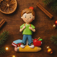 Load image into Gallery viewer, Decorative figurine of a boy with books and an apple on a wooden surface with Christmas decorations.
