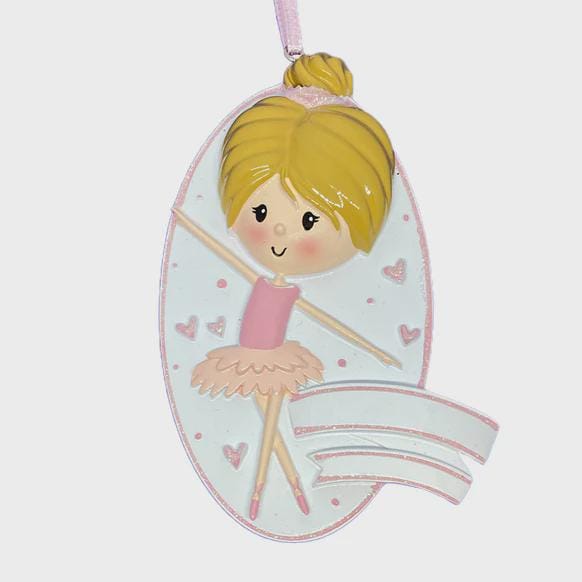 Personalized ballet girl Christmas ornament featuring a cute ballerina character in a pink tutu dress with heart details, customizable name area on the front banner and customizable year area below, glossy finish with raised 3D front details and flat 2D back, white hanging ribbon, displayed on a snowy holiday background with pine branches and festive decorations.