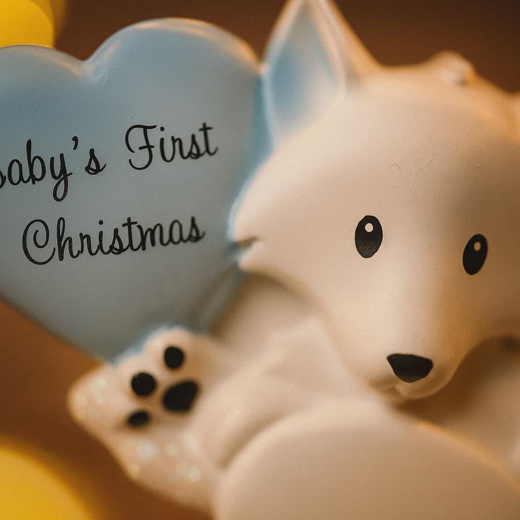 Polar bear figurine holding a heart-shaped 'Baby's First Christmas' ornament.
