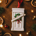 Load image into Gallery viewer, Decorative Christmas ornament resembling a door with wreaths and a bow, surrounded by festive items on a wooden surface.
