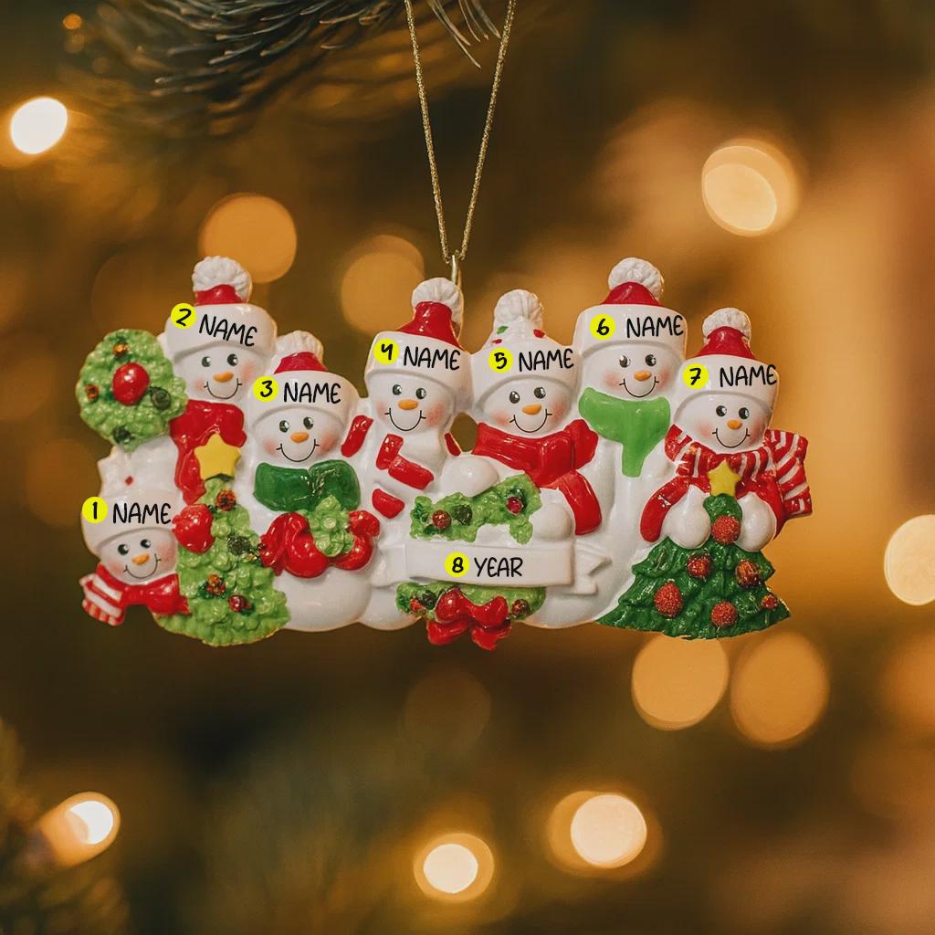 Personalized snowman family Christmas ornament with name tags on a blurred Christmas tree background.