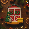 Load image into Gallery viewer, Decorative Christmas ornament resembling a red barn with wreaths, trees, and a lantern on a wooden surface with festive decorations.
