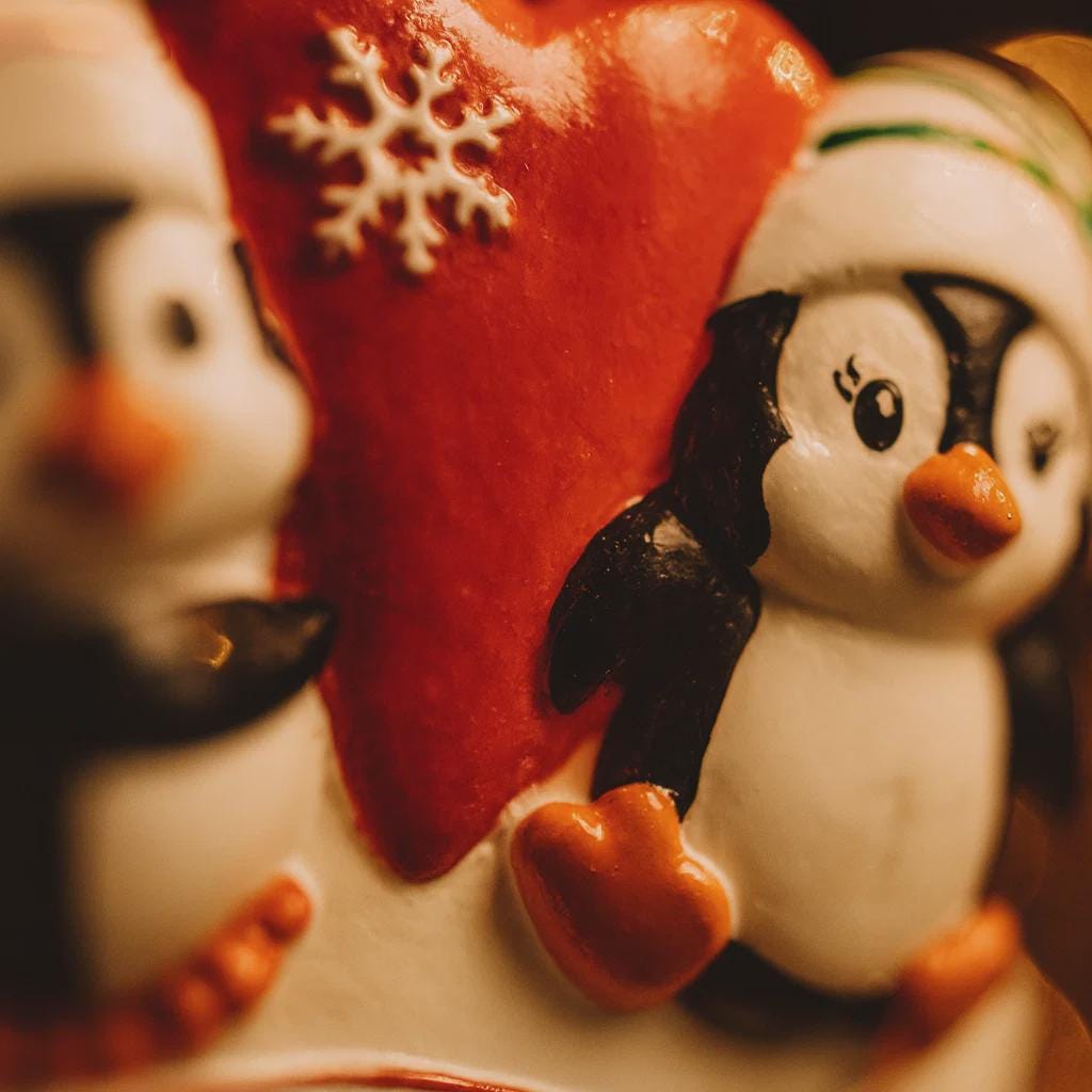 Two penguin figurines in front of a red heart with a snowflake, on a blurred background.