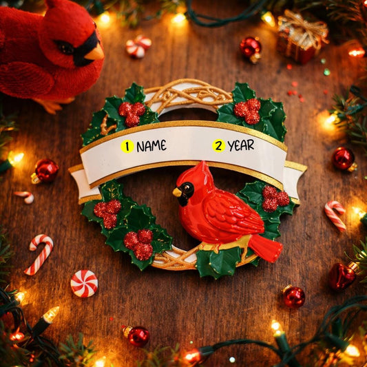 Personalized cardinal wreath ornament featuring a vibrant red cardinal bird surrounded by green holly leaves and red berries. Designed with a smooth glossy finish and a raised 3D front with a flat back for easy hanging. Includes free handwritten personalization with one name and year displayed on the banner at the top. Styled in a warm festive holiday setting with soft Christmas lights candy details and seasonal decor. A meaningful Christmas tree ornament symbolizing remembrance love and connection perfect 