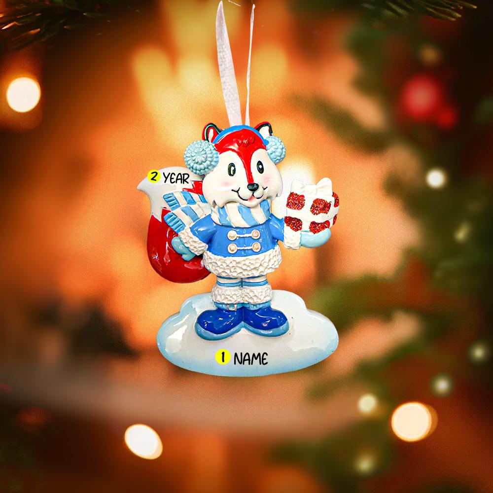 Christmas ornament with a fox character holding a gift, against a blurred Christmas tree background.