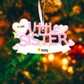 Load image into Gallery viewer, A personalized Little Sister ornament featuring soft pink layered lettering with heart accents and floral details. Designed in gentle pastel tones with a smooth resin finish and subtle glitter highlights. The ornament includes handwritten personalization with a baby name and year, created as a mostly 2D ornament with raised 3D details on the front only. Lightweight and easy to hang, perfect for celebrating a new baby sister and her first Christmas.

