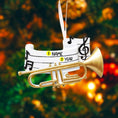 Load image into Gallery viewer, Personalized music ornament featuring a white musical staff design with black notes and a gold trumpet detail. Includes free handwritten personalization with one name and year written on the sheet music. Shown hanging with a ribbon in a warm festive holiday setting with soft lights instruments and seasonal decor. Designed with a 3D raised front and flat back perfect for Christmas tree display and gifts for musicians music lovers and band members.
