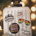 Load image into Gallery viewer, Silver suitcase with travel-themed stickers against a blurred light background
