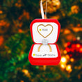 Load image into Gallery viewer, Personalized engagement ring ornament featuring a red velvet style ring box design with a sparkling diamond ring inside. The ornament includes free handwritten personalization with one name and year displayed inside the box. Designed with a smooth glossy finish and elegant gold details. Shown hanging with a ribbon in a festive holiday setting with snow greenery and warm lights. A romantic keepsake ornament perfect for Christmas trees engagements proposals and meaningful gift displays.

