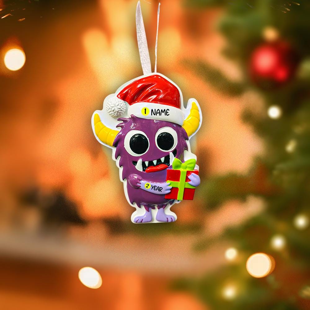 Purple monster Christmas ornament with Santa hat and gift, blurred Christmas tree background