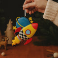 Load image into Gallery viewer, Colorful rocket-shaped ornament held by a hand with a dark background

