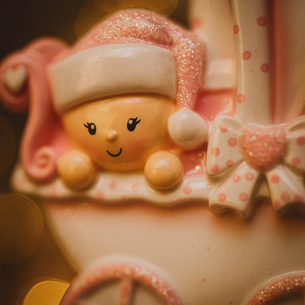 Personalized baby girl Christmas ornament featuring a soft pink stroller with glitter details and a smiling baby wearing a pink nightcap. Custom name appears on the top and year on the bottom, making it a perfect Baby’s First Christmas keepsake. This pink resin holiday ornament is ideal for newborn girls, baby shower gifts, and celebrating a special first Christmas memory.
