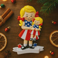 Load image into Gallery viewer, Decorative Christmas ornament of two girls in American flag dresses on a festive background.
