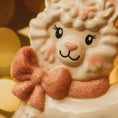 Load image into Gallery viewer, A glossy resin baby girl llama ornament features a white smiling llama with soft pink accents, raised textured fur details, pink bow and scarf elements, glitter highlights, and a smooth painted cartoon style finish, styled with warm holiday lights and nursery themed props, handwritten personalization showing the baby name on the front banner and the year placed on the llama body, designed as a mostly 2D ornament with raised 3D details on the front only.
