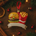 Load image into Gallery viewer, Hamburger and french fries ornament with a red ribbon on a wooden surface with Christmas decorations.
