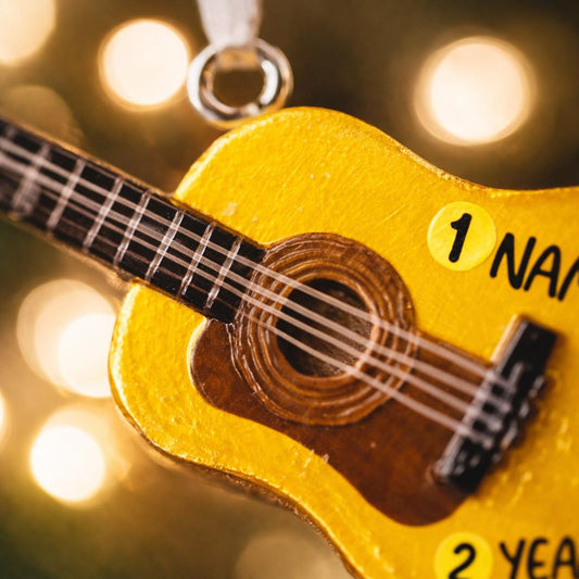 Personalized guitar ornament featuring a classic acoustic guitar design with detailed strings and wood texture. Custom name and year handwritten directly on the guitar body. High detail 3D resin ornament with white hanging ribbon. Perfect Christmas tree decoration for guitar players musicians music lovers and acoustic guitar fans. Warm musical theme ideal for holiday decor and meaningful personalized gifts.